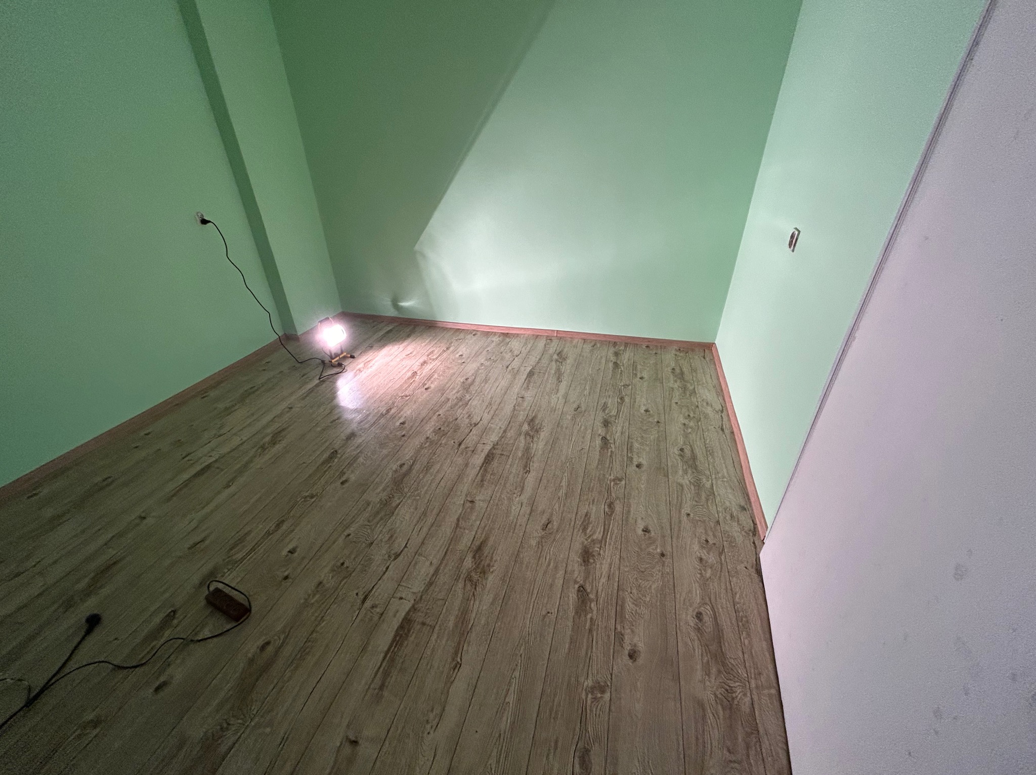 Ukończona podłoga z paneli w pokoju z pomalowanymi na zielono ścianami i sufitem, oświetlona lampą roboczą, widok z dołu, ukazujący efekt ułożenia.