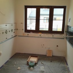 TymiRękami - Wnętrze w trakcie układania płytek z poziomowaniem. Widoczne metalowe profile, krzyżyki dystansowe i przewody elektryczne. Okno z drewnianą ramą. Folia ochronna na podłodze.