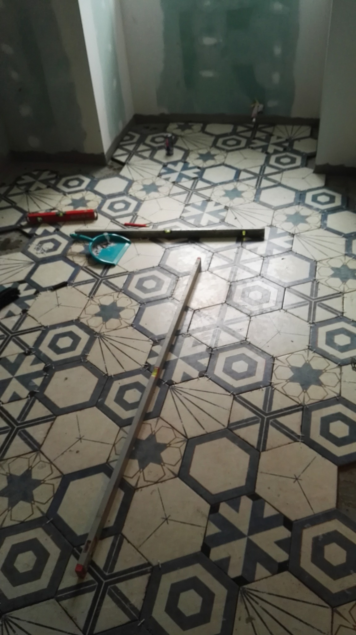 Układanie heksagonalnych płytek podłogowych w łazience, z widocznymi narzędziami: poziomica, szpachelka. Ściany przygotowane pod wykończenie.