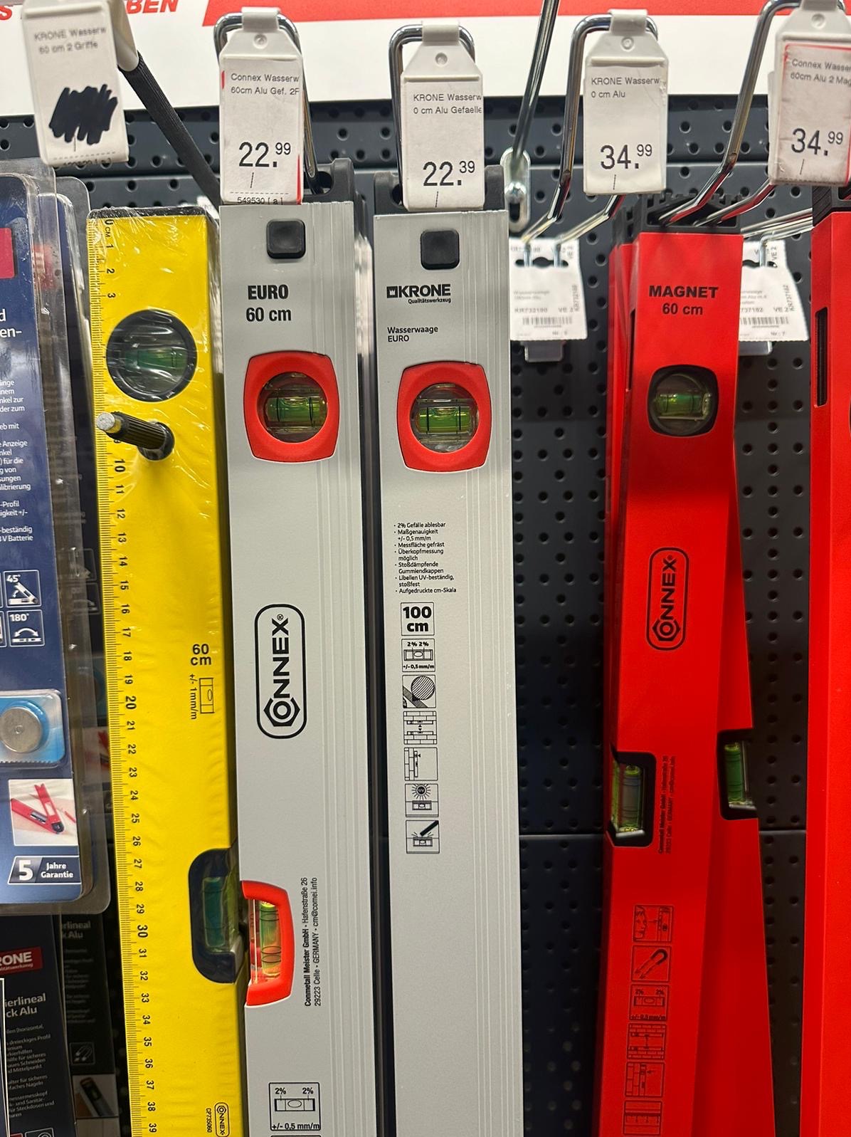 Różnokolorowe poziomice marki Onnex i Krone, z etykietami cenowymi, wiszą na perforowanej ścianie w sklepie. Widoczne skale i libelle.