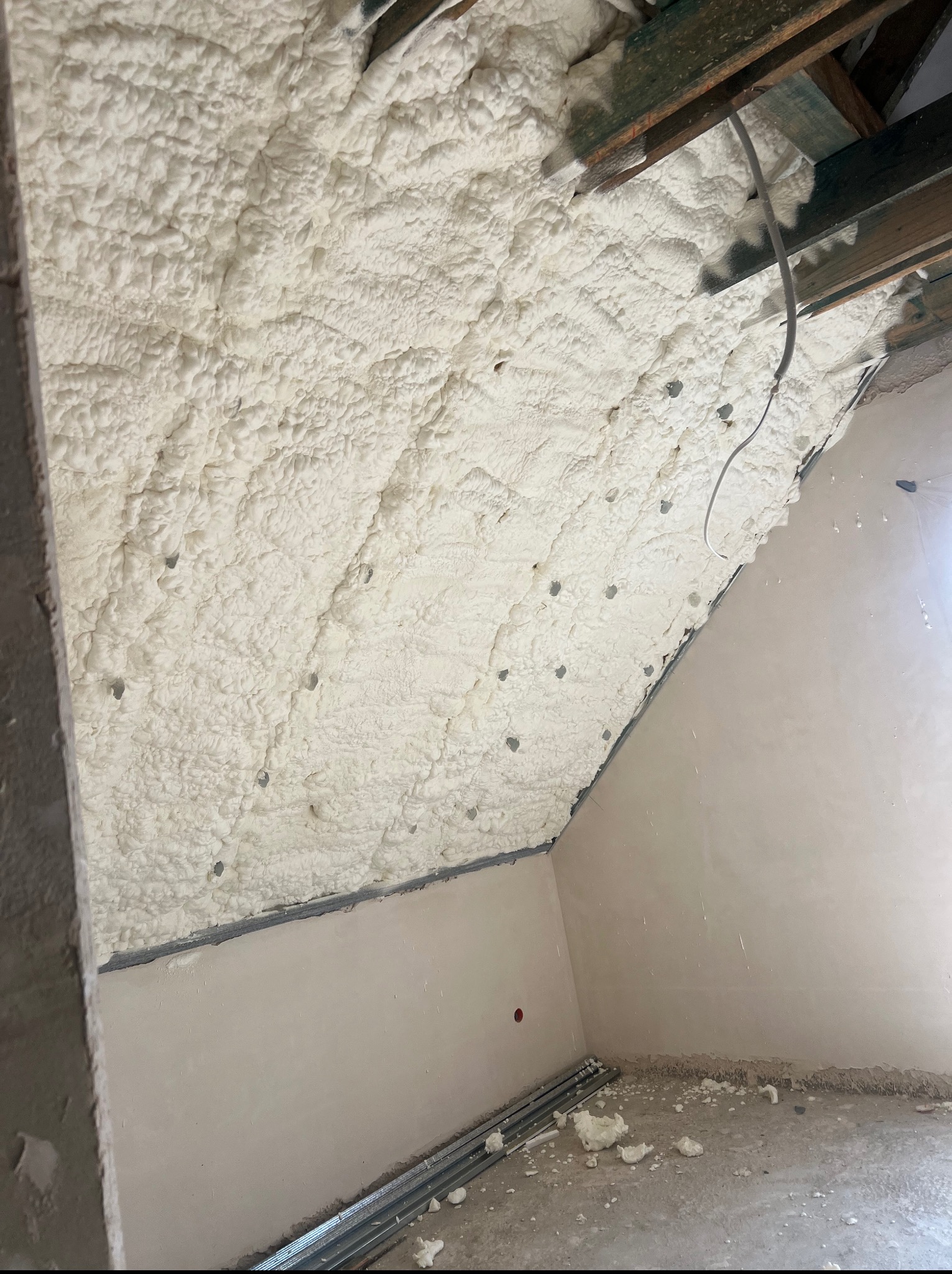 Poddasze po ociepleniu pianką PUR. Widoczne drewniane belki stropowe i równomiernie nałożona pianka. Na podłodze fragmenty pianki i profile.