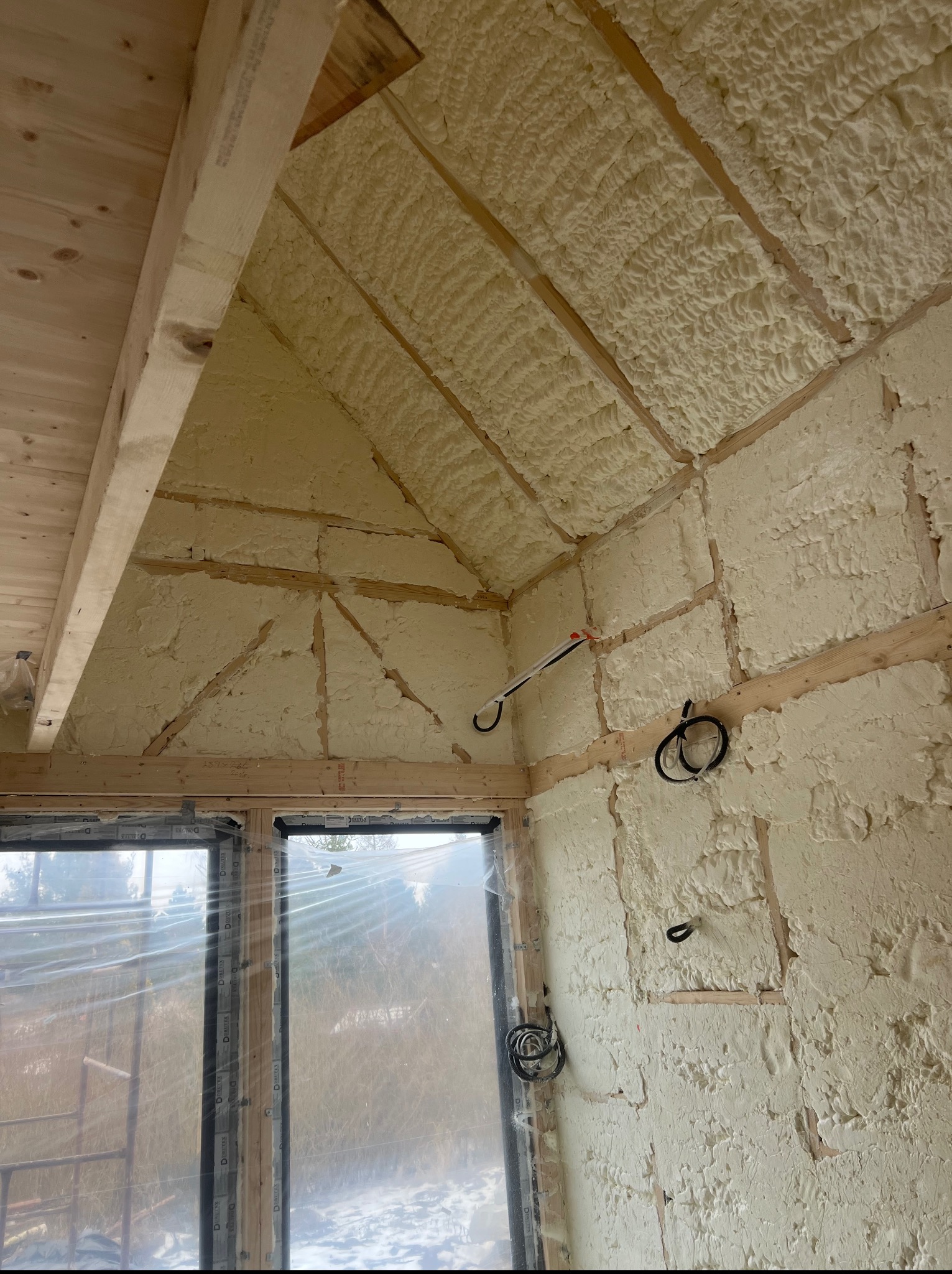 Poddasze z ociepleniem pianką PUR, widoczne drewniane elementy konstrukcyjne i instalacja elektryczna. Okno zabezpieczone folią.