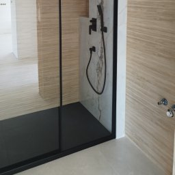 REM-NOV Michał Nowacki - Nowoczesna kabina prysznicowa z czarną armaturą i płytkami imitującymi drewno. Minimalistyczny design, jasne kolory i eleganckie wykończenie.