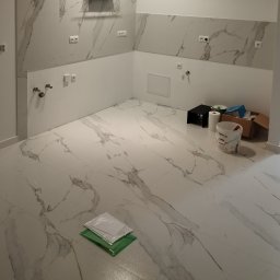 REM-NOV Michał Nowacki - Wykończona łazienka z marmurowymi płytkami na ścianach i podłodze. Widoczne puszki elektryczne, instalacja wodna i akcesoria malarskie. Nowoczesny design.