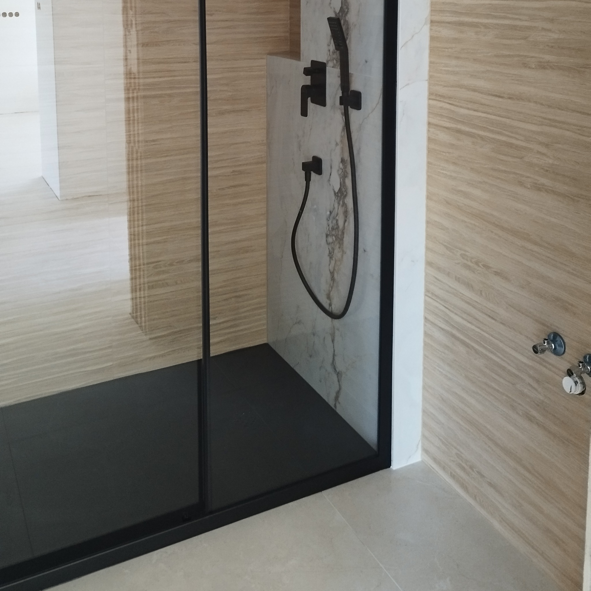 Nowoczesna kabina prysznicowa z czarną armaturą i płytkami imitującymi drewno. Minimalistyczny design, jasne kolory i eleganckie wykończenie.