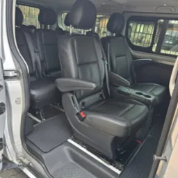 Wnętrze busa z czarnymi skórzanymi fotelami, widok z otwartych drzwi. Podłoga wyłożona gumową matą, widoczne zagłówki i podłokietniki.