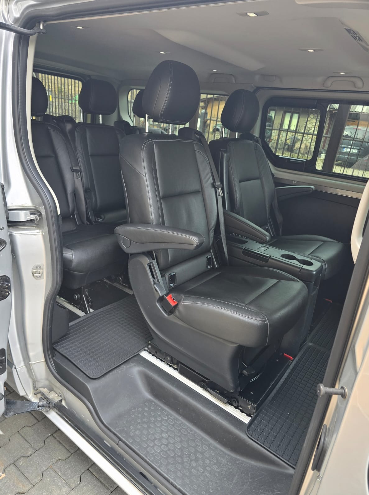 Wnętrze busa z czarnymi skórzanymi fotelami, widok z otwartych drzwi. Podłoga wyłożona gumową matą, widoczne zagłówki i podłokietniki.