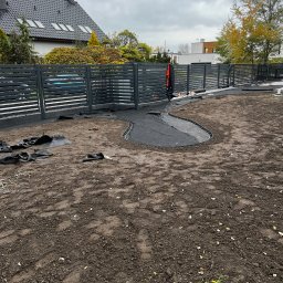 Bracia ogrodnicy. - Przygotowanie terenu pod trawnik z rolki we Wrocławiu. Widoczne czarne maty i obrzeża rabat na przygotowanej ziemi. W tle nowoczesne ogrodzenie i dom.