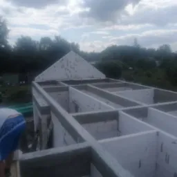 Budowa domu z betonu komórkowego: ściany parteru, widoczny dekarz przy pracy, tło z zielenią. Kąt widzenia z góry, pochmurne niebo.