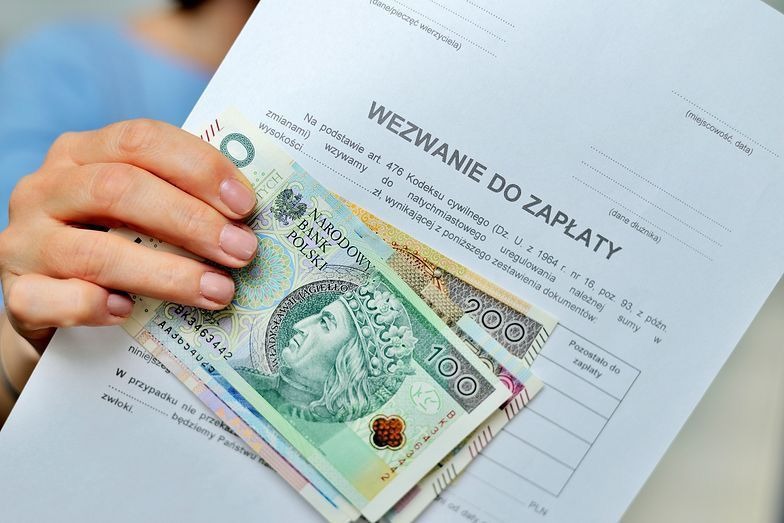 Wezwanie do zapłaty z banknotami 100 i 200 zł w dłoni, skierowane do dłużnika. Dokument z tekstem prawnym i miejscem na dane. Finanse i zobowiązania.