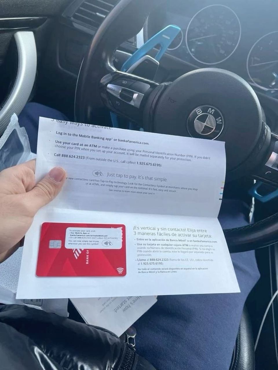 Aktywacja karty płatniczej Bank of America w samochodzie BMW. Ulotka informacyjna z kartą na tle kierownicy i deski rozdzielczej.
