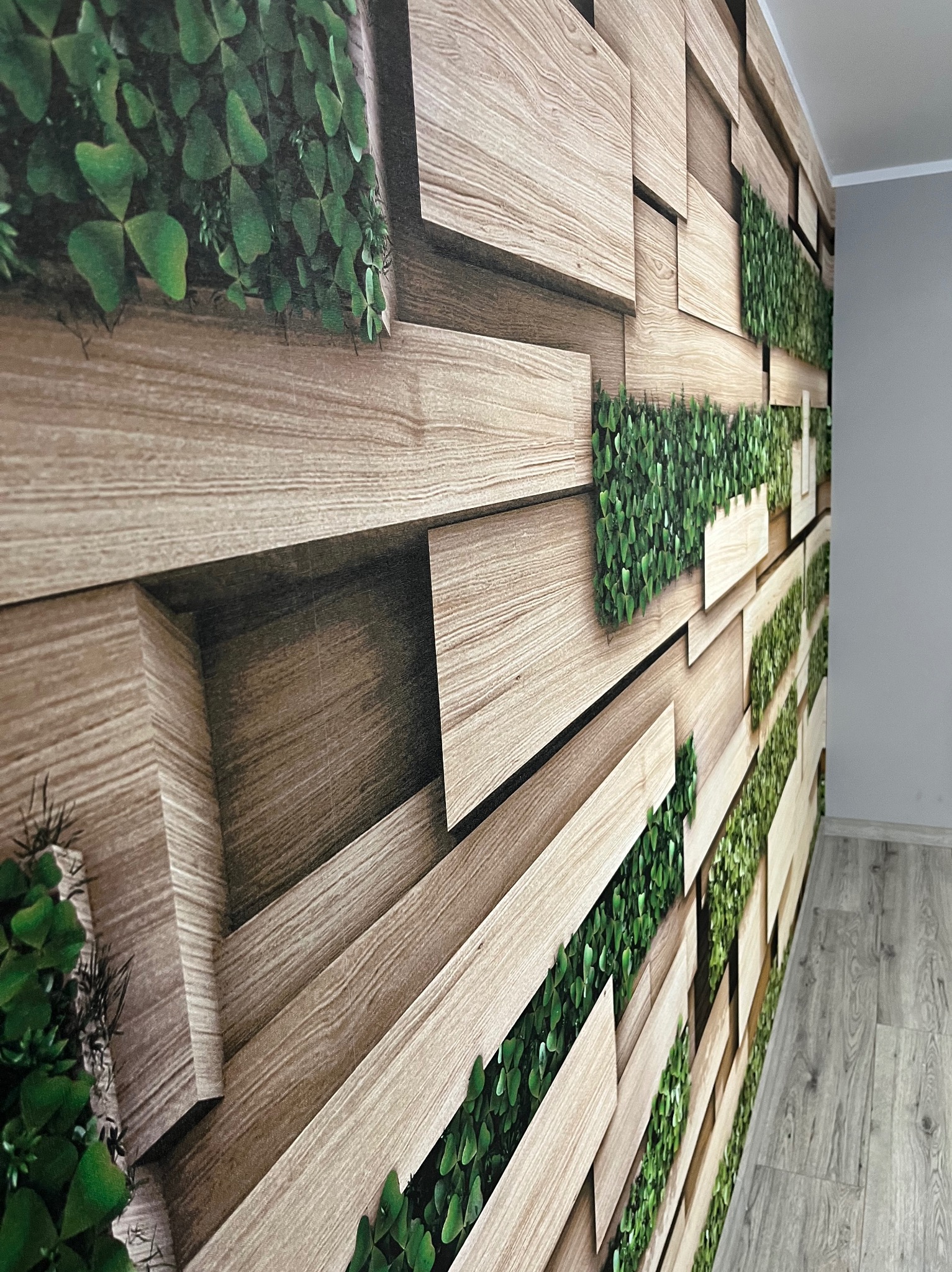 Dekoracyjna ściana z drewnianymi panelami 3D i zielonymi roślinami, tworząca unikalny wystrój wnętrza. Perspektywa z boku ukazuje strukturę i głębię.