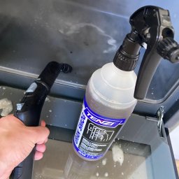 Twój Porządek - Czyszczenie piekarnika parownicą i detergentem Tenzi Gran Smog, widoczne krople płynu na szklanych drzwiach piekarnika podczas usuwania zabrudzeń.