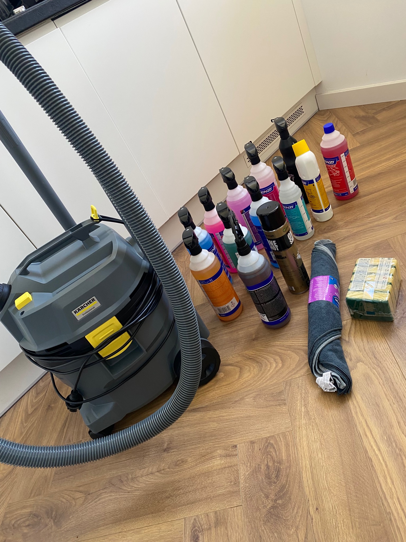 Profesjonalny odkurzacz Karcher, środki czystości w butelkach, gąbki i ściereczki na drewnianej podłodze, gotowe do użycia podczas sprzątania.