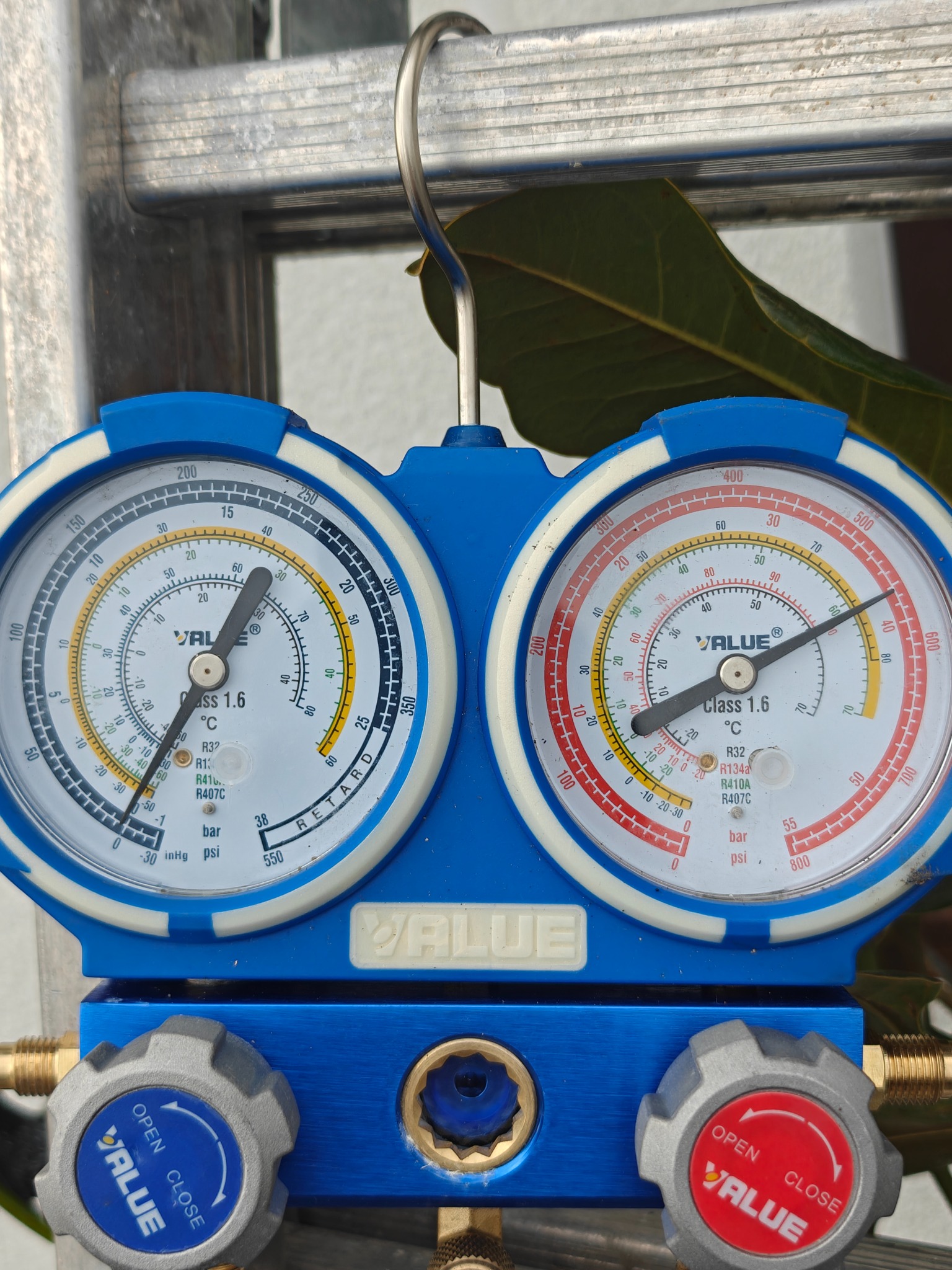 Manometry VALUE na drabinie, z widocznymi wskazaniami ciśnienia i oznaczeniami czynników chłodniczych. Widoczne zawory regulacyjne z oznaczeniami 'Open' i 'Close'.