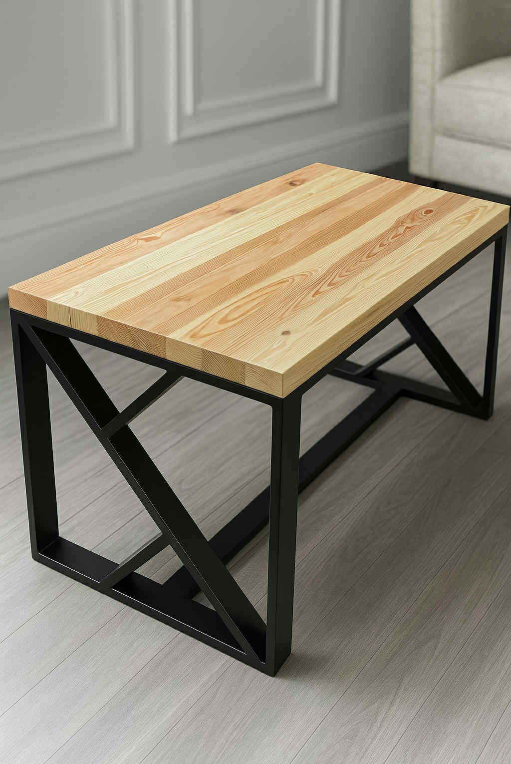 Stolik kawowy z jasnego drewna z wyraźnym usłojeniem na blacie i czarną, metalową podstawą o geometrycznym kształcie, stojący na drewnianej podłodze.