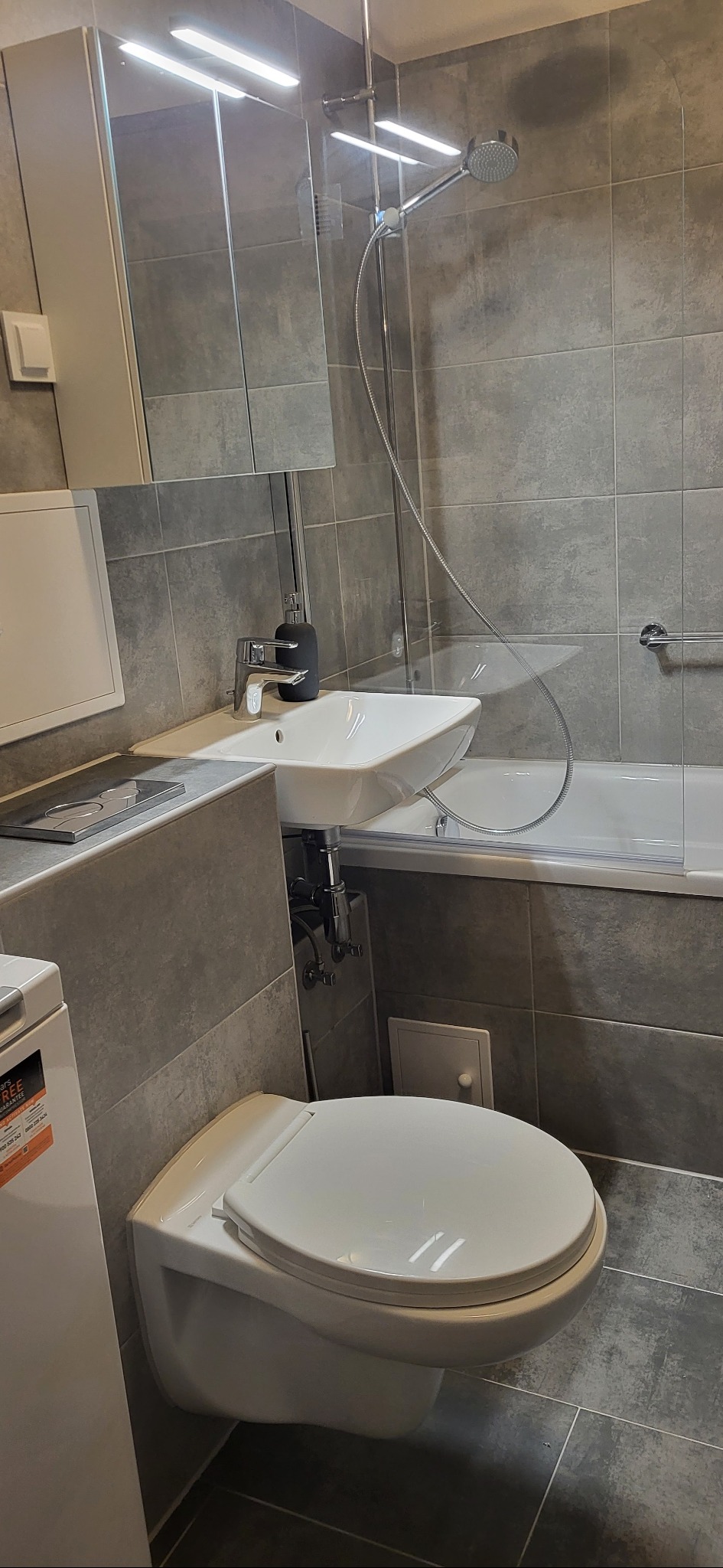 Nowoczesna łazienka z szarymi płytkami, podwieszaną toaletą i umywalką nablatową. Minimalistyczny design, oświetlenie LED i chromowana armatura.