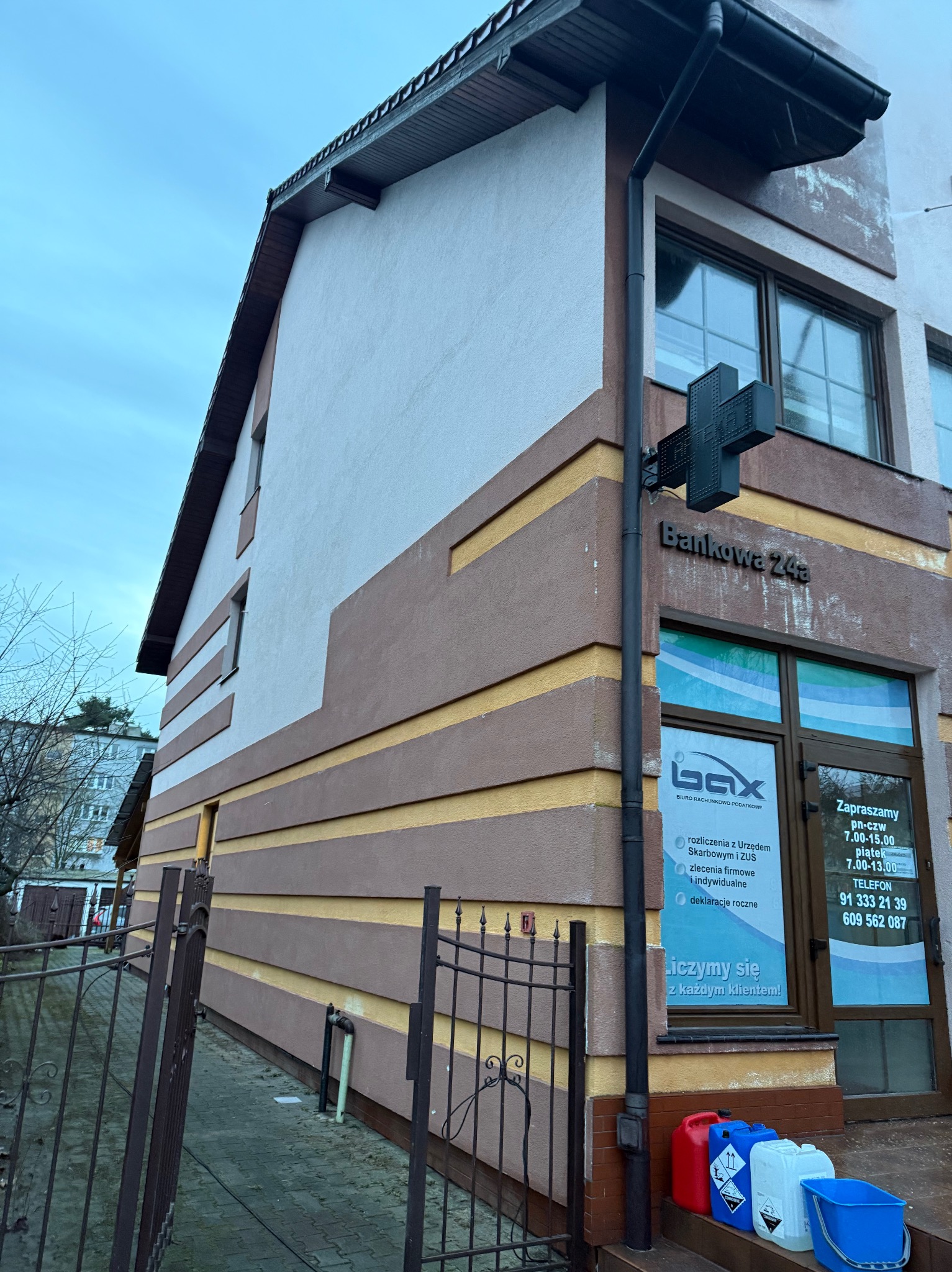 Elewacja budynku biurowego po malowaniu, z widocznymi pojemnikami z farbą. Utrzymana kolorystyka w odcieniach beżu i brązu z żółtymi akcentami.