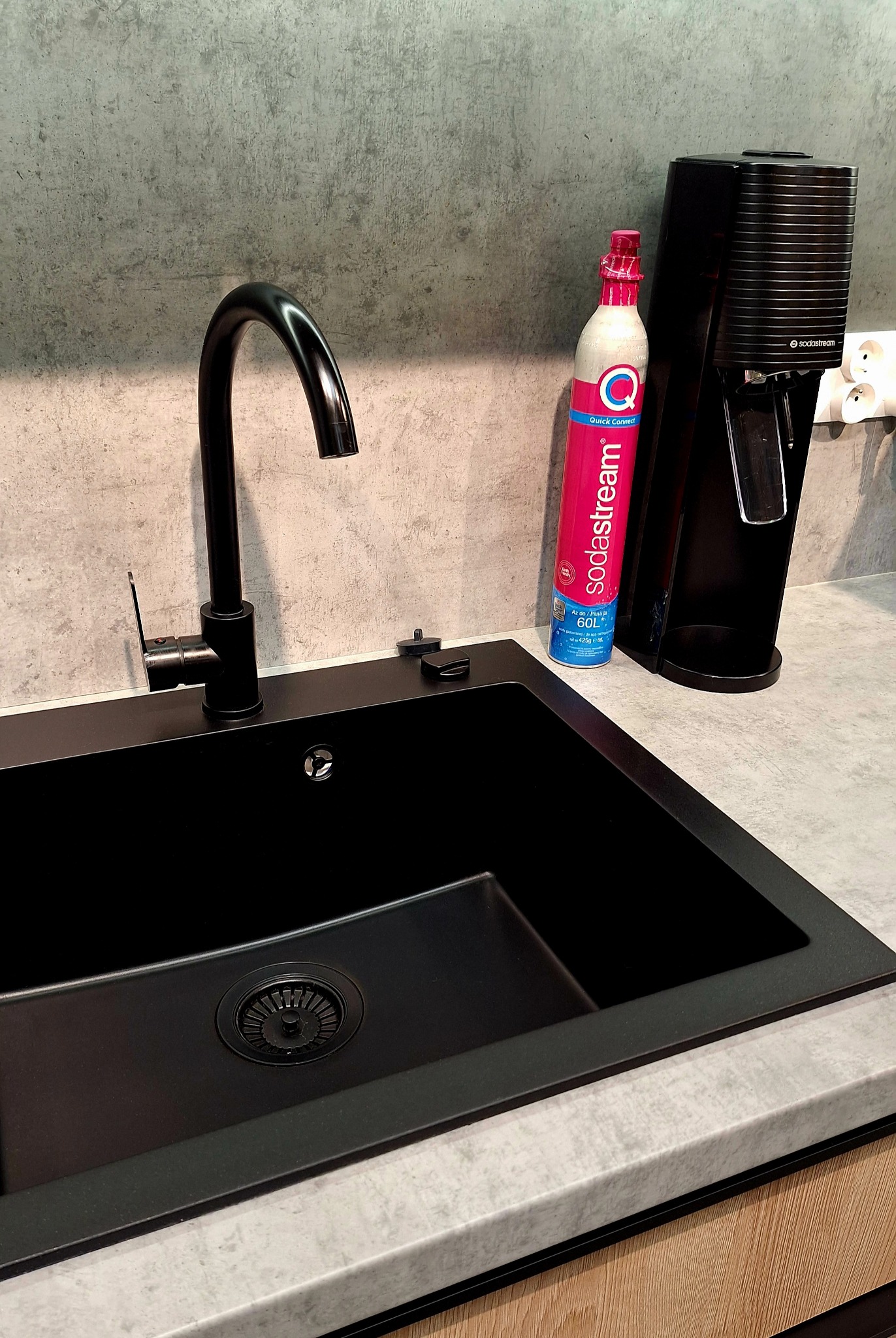 Czarny, minimalistyczny zlew z baterią i saturatorem SodaStream na blacie o betonowej fakturze. Nowoczesne wykończenie kuchni.