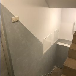 Usługi wykończeniowe- Robert Nadolski - Klatka schodowa po remoncie: ściany pomalowane w dwóch odcieniach szarości, z widocznymi schodami i drzwiczkami rewizyjnymi. Nowoczesne wykończenie.