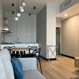 Usługi wykończeniowe- Robert Nadolski - Nowoczesne wnętrze mieszkania z drewnianą podłogą, szarą zabudową kuchenną i okrągłym stołem. Minimalistyczny design z wiszącymi lampami kulami.