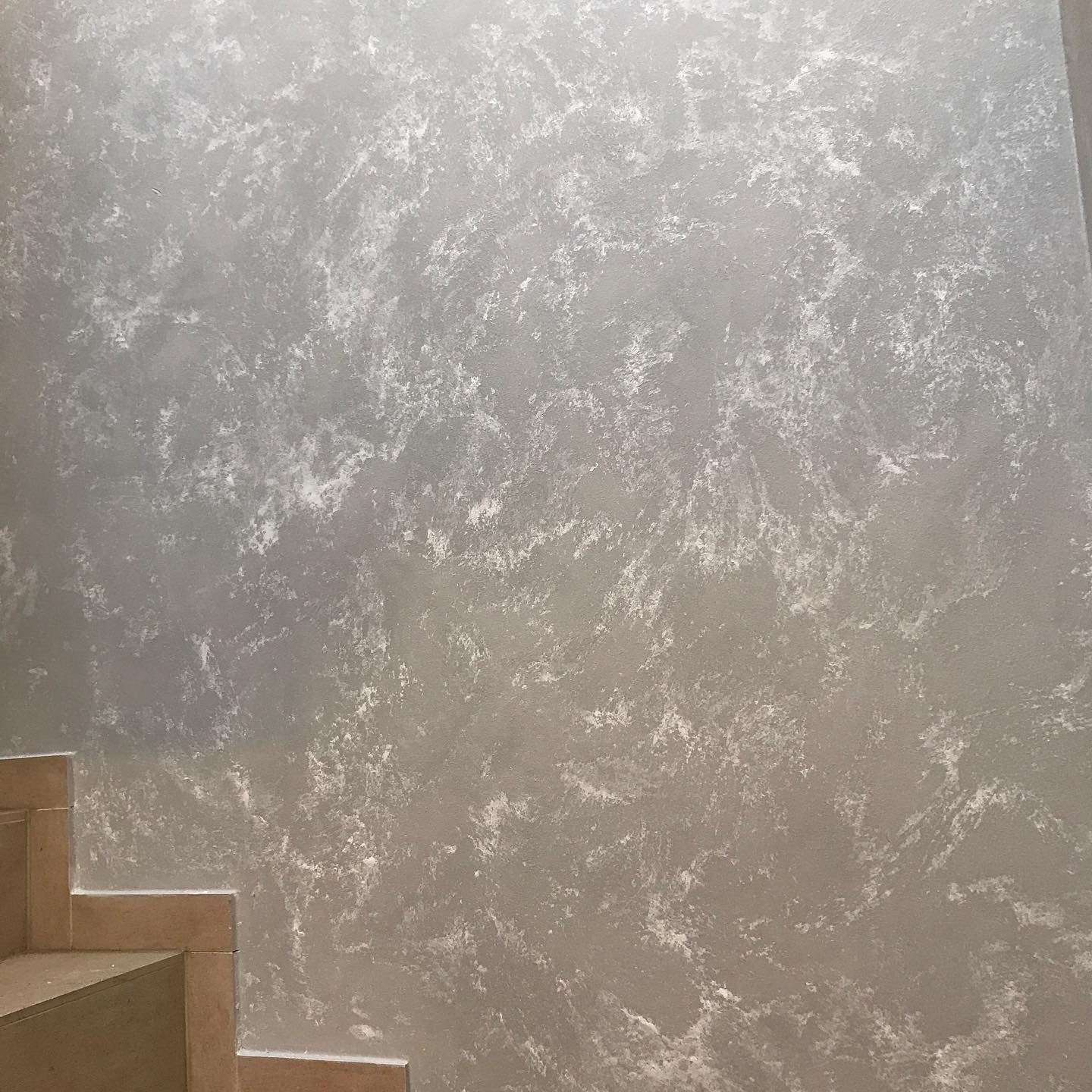 Ściana w odcieniach szarości z dekoracyjną fakturą, widoczne fragmenty schodów. Efektowna aranżacja wnętrza, nowoczesny design.