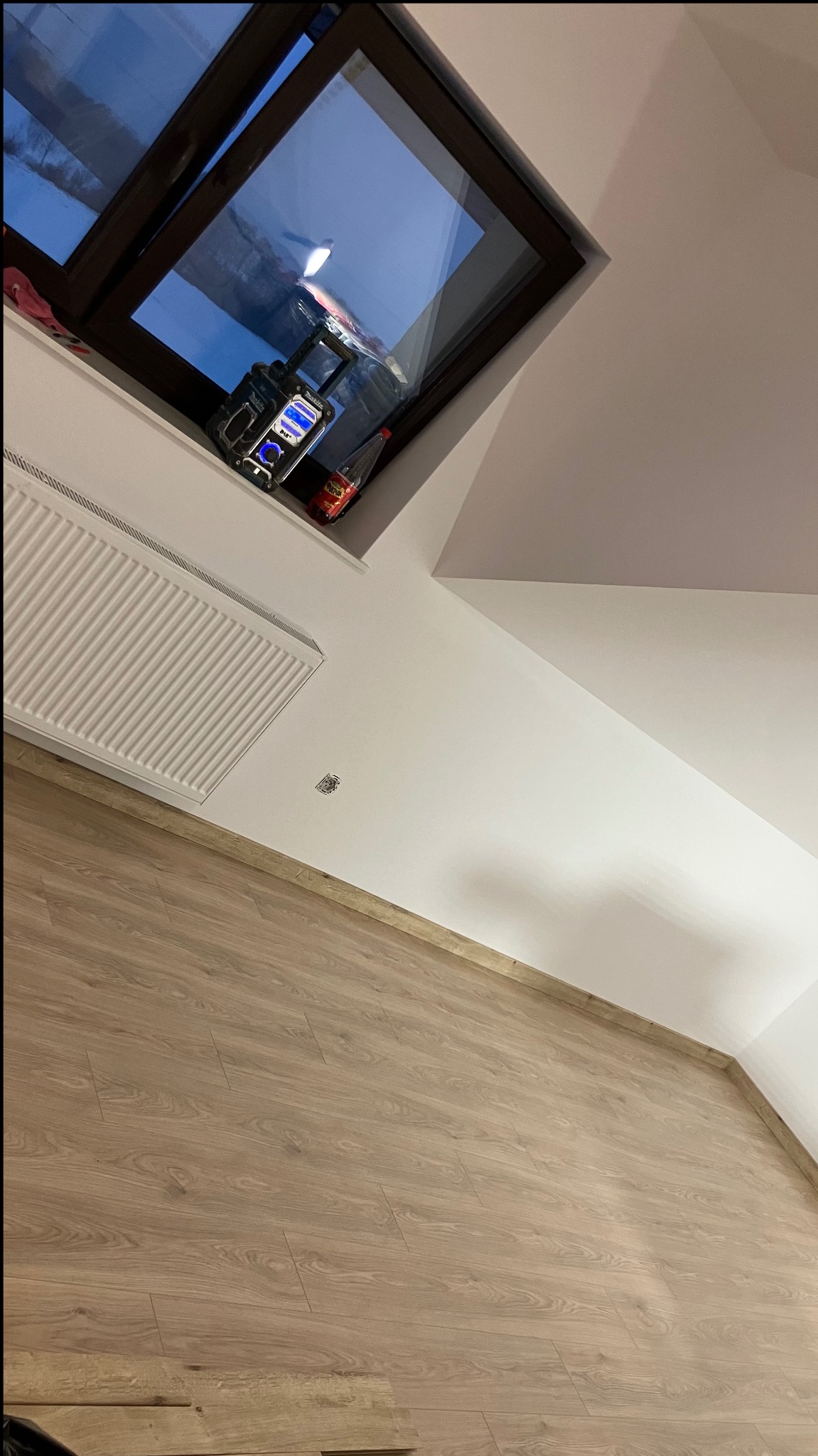 Jasne panele podłogowe w pokoju na poddaszu, widok na okno dachowe z radiem budowlanym i napojem. Świeżo pomalowane ściany i grzejnik.