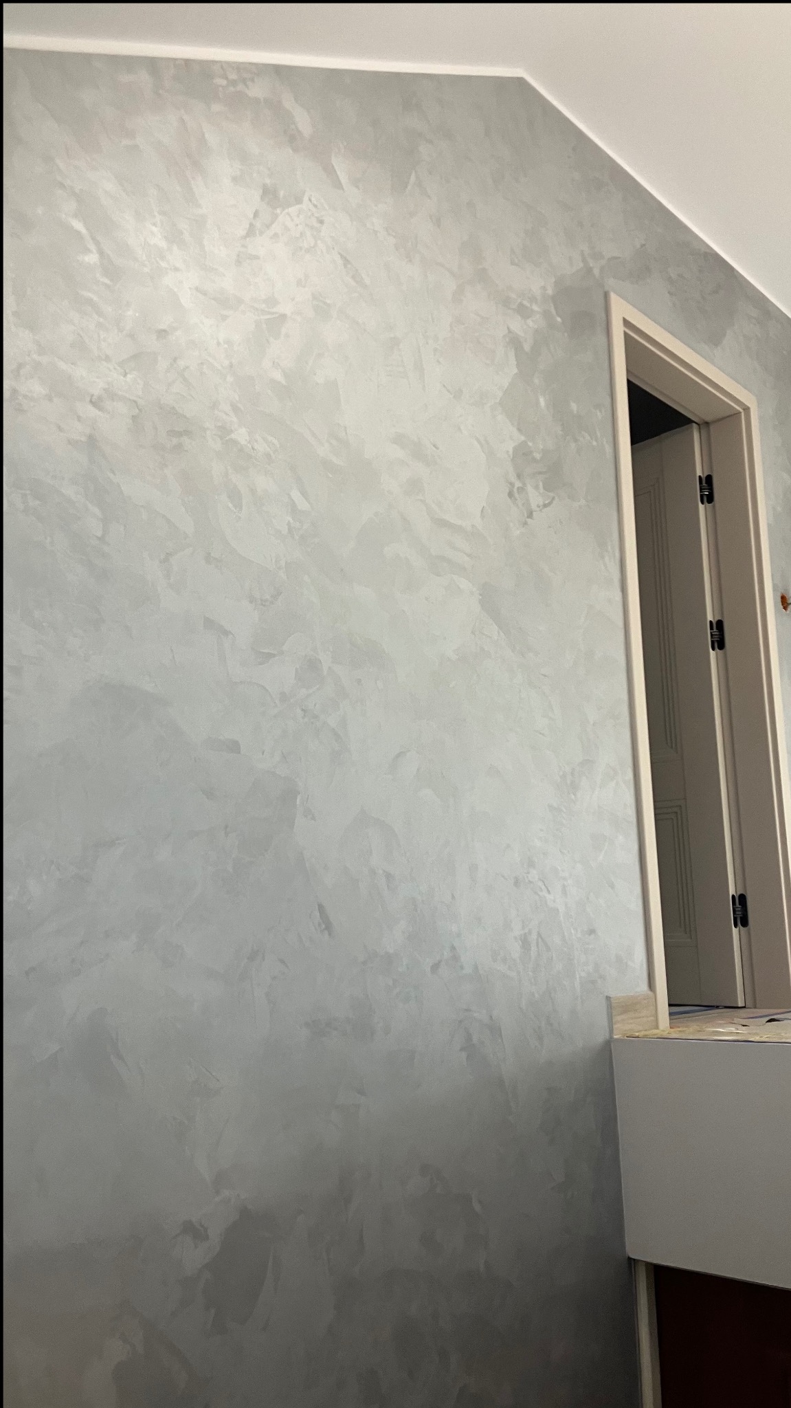 Ściana z efektem dekoracyjnym w odcieniach szarości, widoczna obok otwartych drzwi. Wykończenie wnętrza z charakterystyczną fakturą.