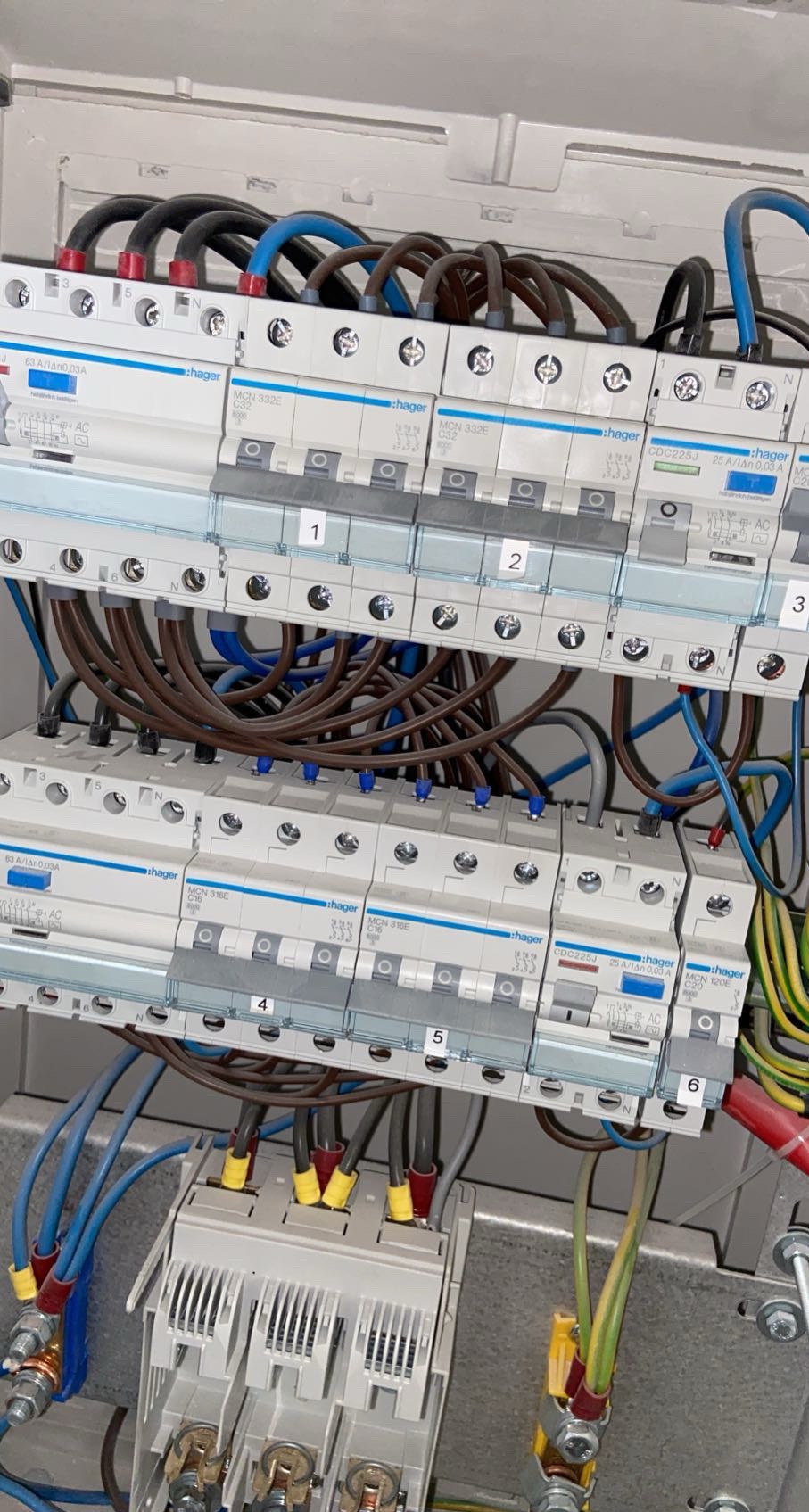 Rozdzielnica elektryczna Hager z numerowanymi bezpiecznikami i precyzyjnie ułożonymi kablami w kolorach: czarnym, niebieskim, brązowym, żółto-zielonym.
