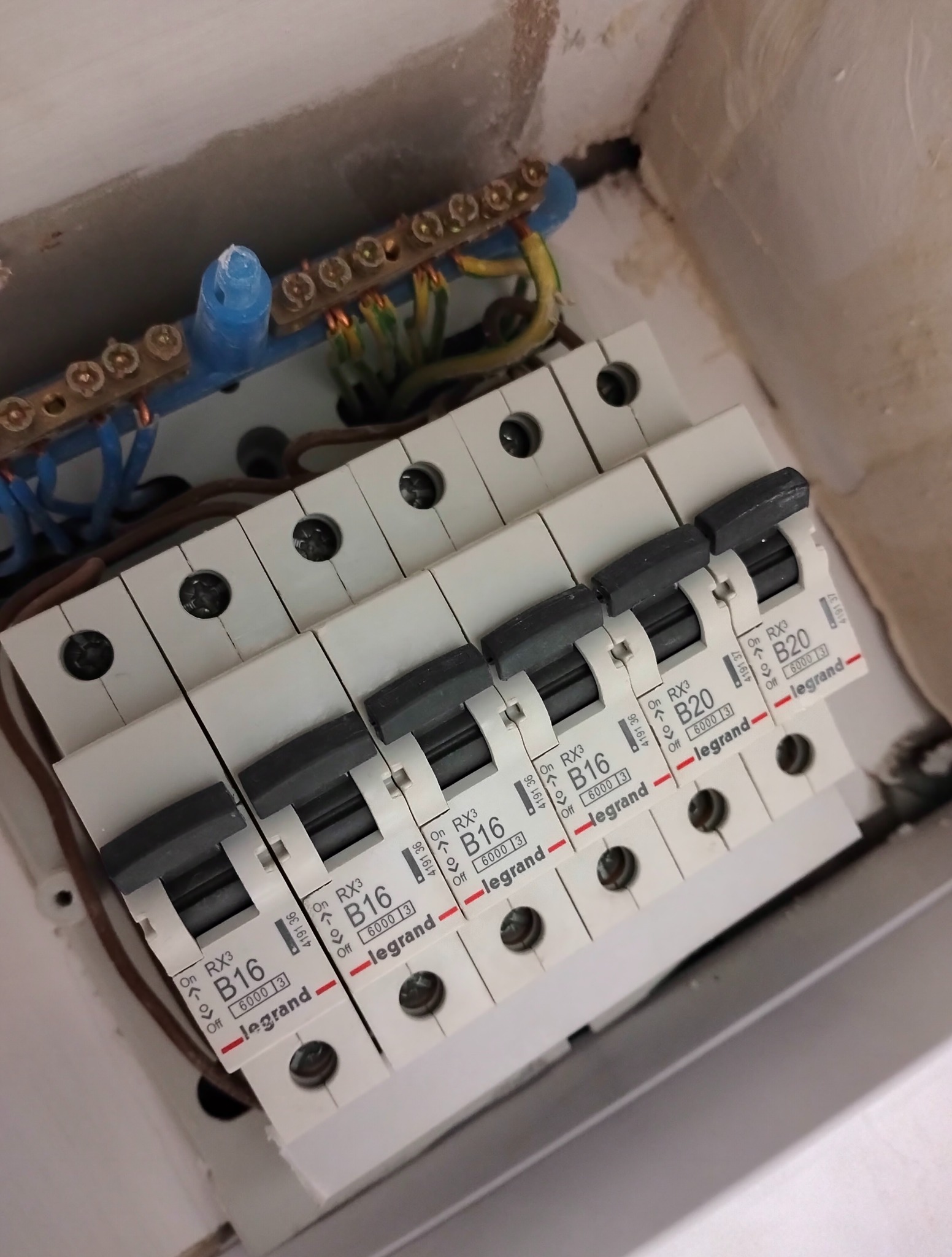 Rozdzielnia elektryczna z zamontowanymi bezpiecznikami Legrand B16 i B20, widoczne przewody i szyny zbiorcze. Instalacja w trakcie prac.