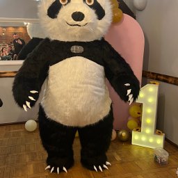 TwojeChwile360 - Panda, maskotka na urodzinach dziecka, stoi obok podświetlanej cyfry '1' i balonów. W tle lustro odbija bawiących się gości.