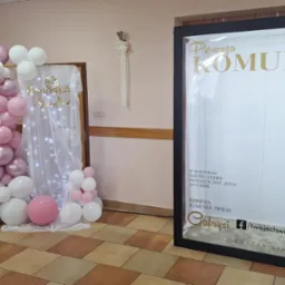 Dekoracja komunijna z balonów w odcieniach różu i bieli, oraz podświetlana ścianka z napisem 'Pierwsza Komunia Święta' i datą 24 maja 2025.