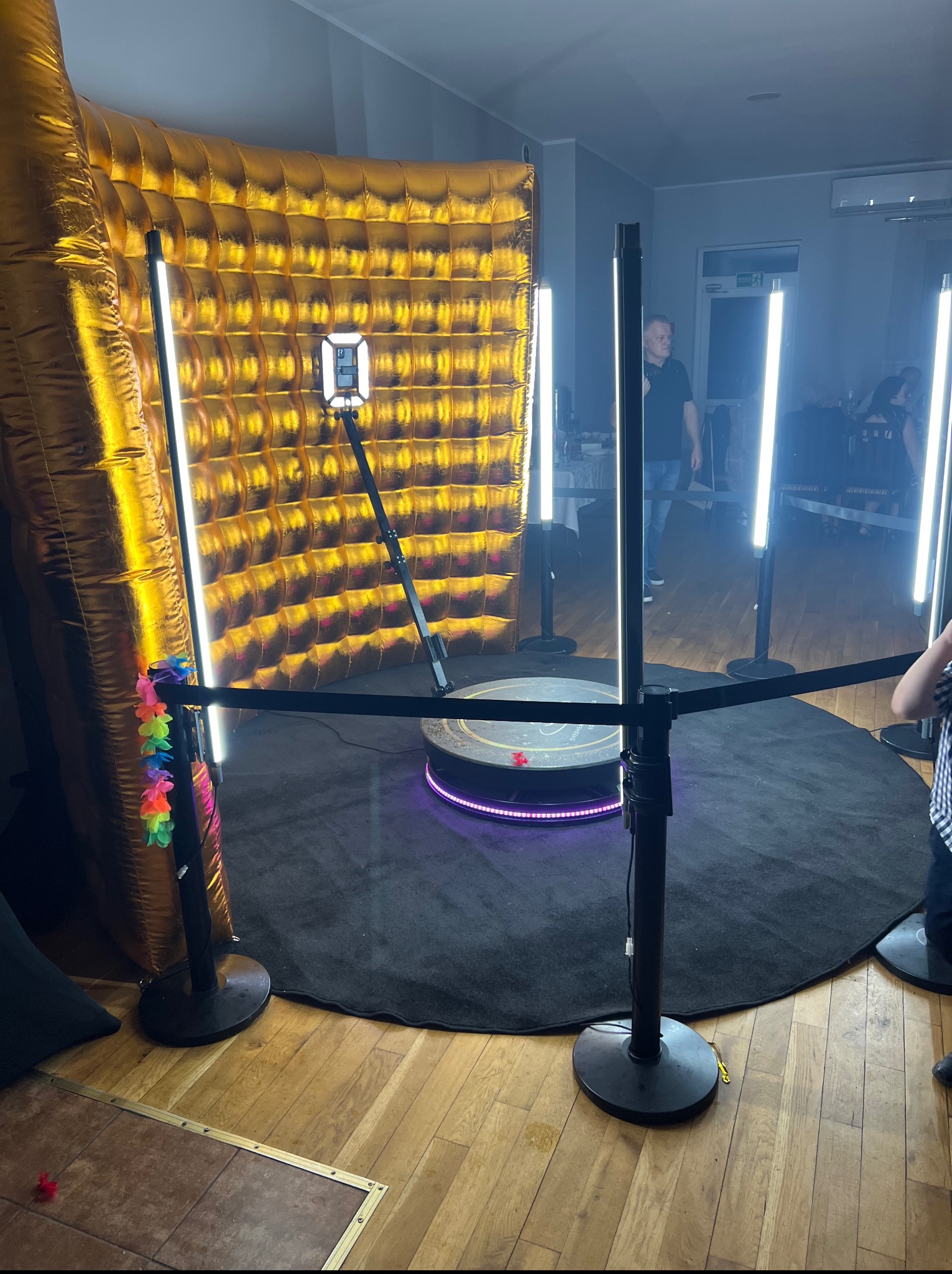 Videobudka 360 z złotym, dmuchanym tłem i oświetleniem LED. Na podłodze czarny dywan i drewniany parkiet. Widoczny fragment osoby.