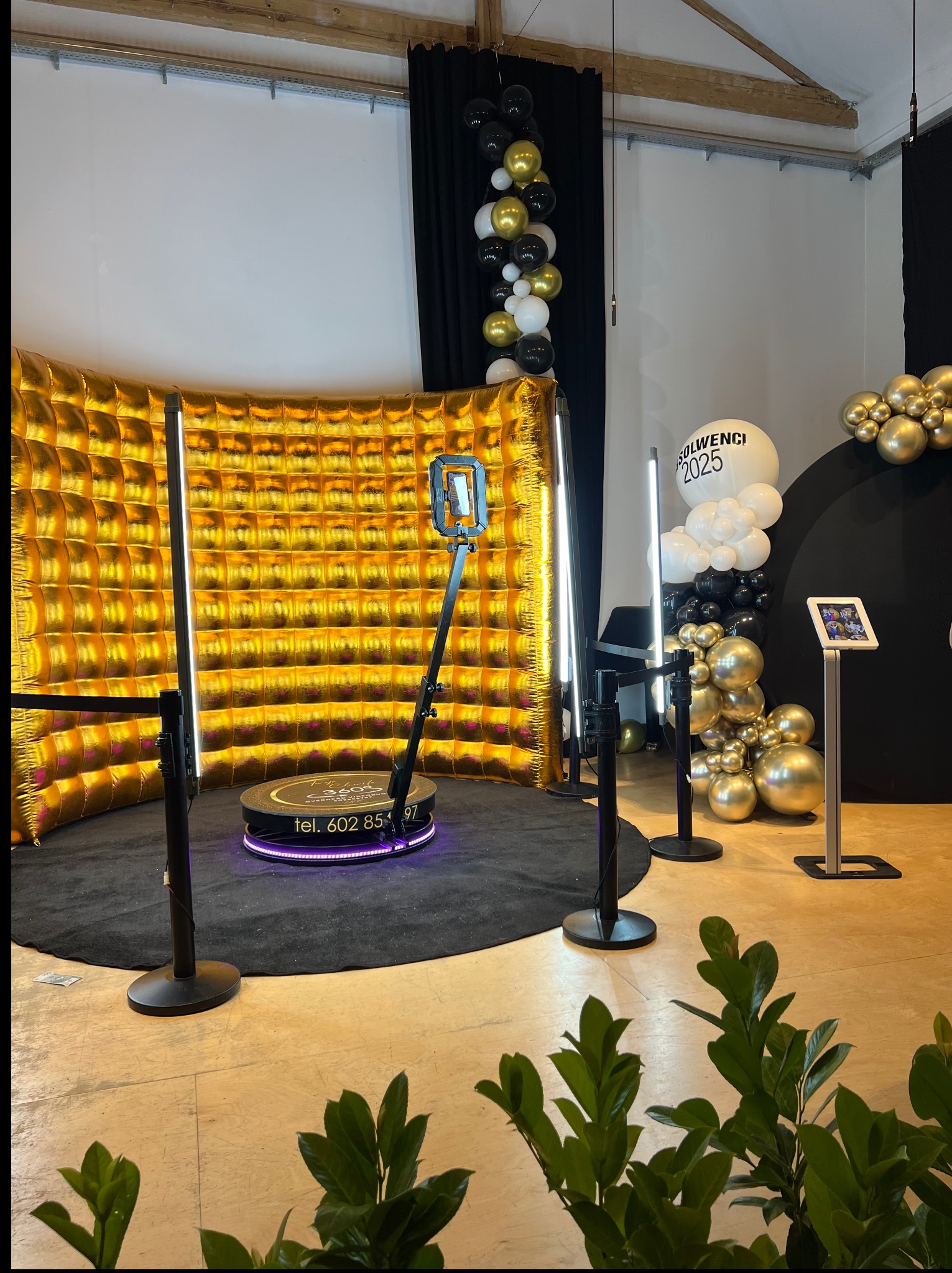 Złota ścianka i obrotowa platforma 360° z oświetleniem LED, tworzące nowoczesną fotobudkę. Dekoracje z balonów w odcieniach złota, czerni i bieli.