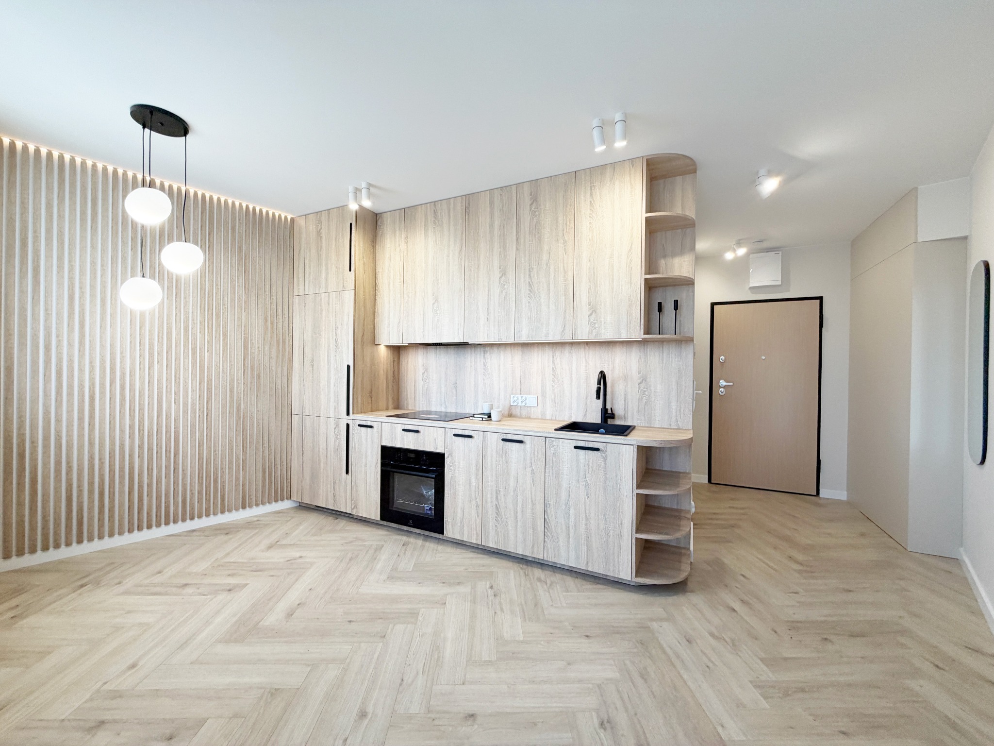 Jasna, nowoczesna kuchnia z drewnianymi frontami i parkietem w jodełkę. Minimalistyczne oświetlenie i zabudowa meblowa tworzą spójną, przestronną aranżację wnętrza.