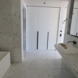 Elegancka łazienka w bieli i szarości z marmurowymi płytkami, minimalistyczną umywalką i zabudową szaf. Wnętrze po remoncie, widok na całe pomieszczenie.