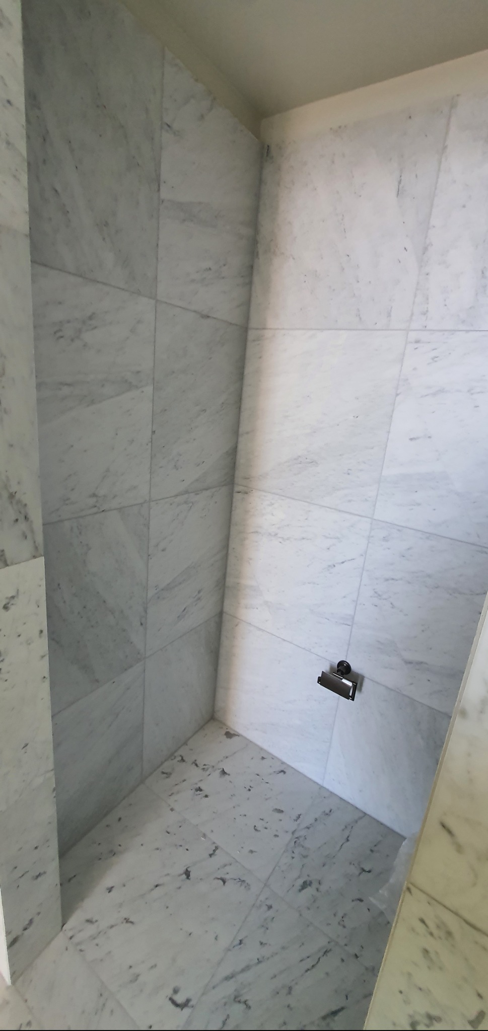 Wnętrze łazienki wyłożone białym marmurem z widocznym uchwytem na papier toaletowy. Minimalistyczny design i eleganckie wykończenie.