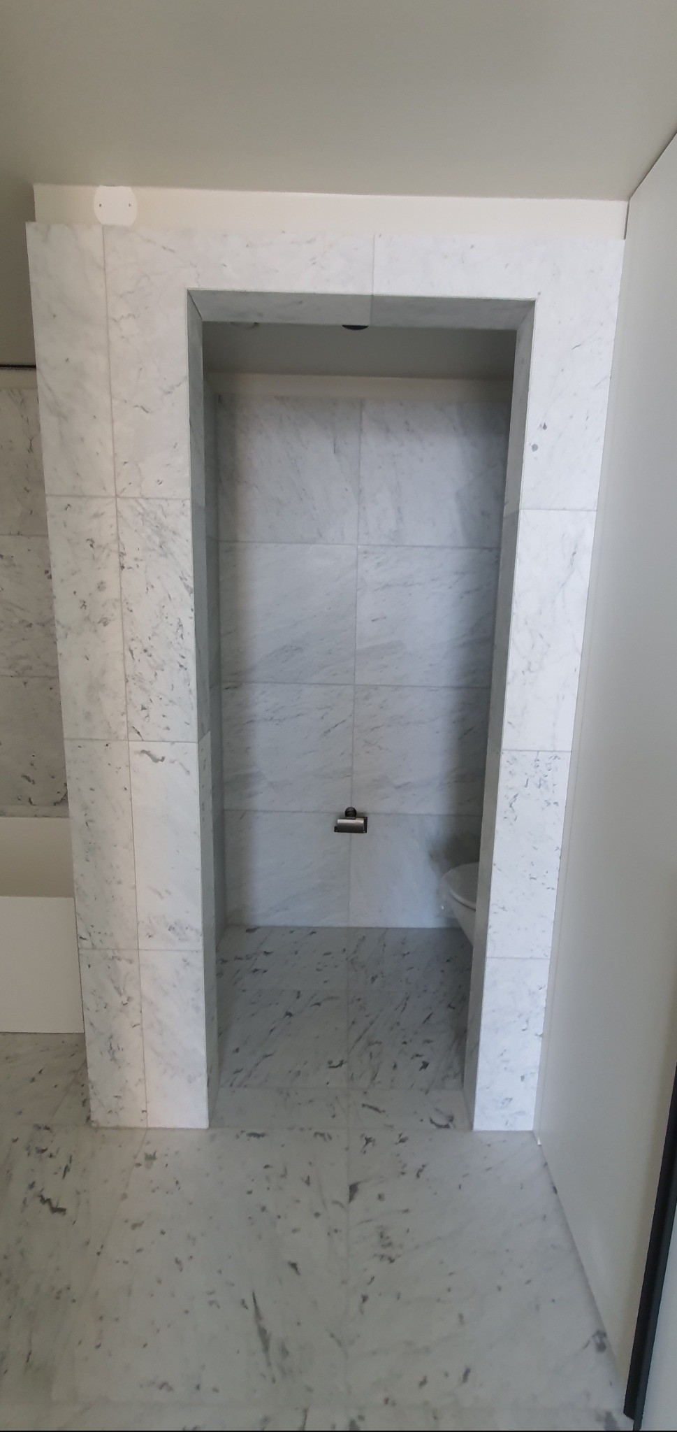 Wykończona wnęka prysznicowa z marmurowymi płytkami, widok od frontu. Nowoczesny design, jasne wnętrze, podkreślone detale wykończeniowe. Minimalistyczny styl.