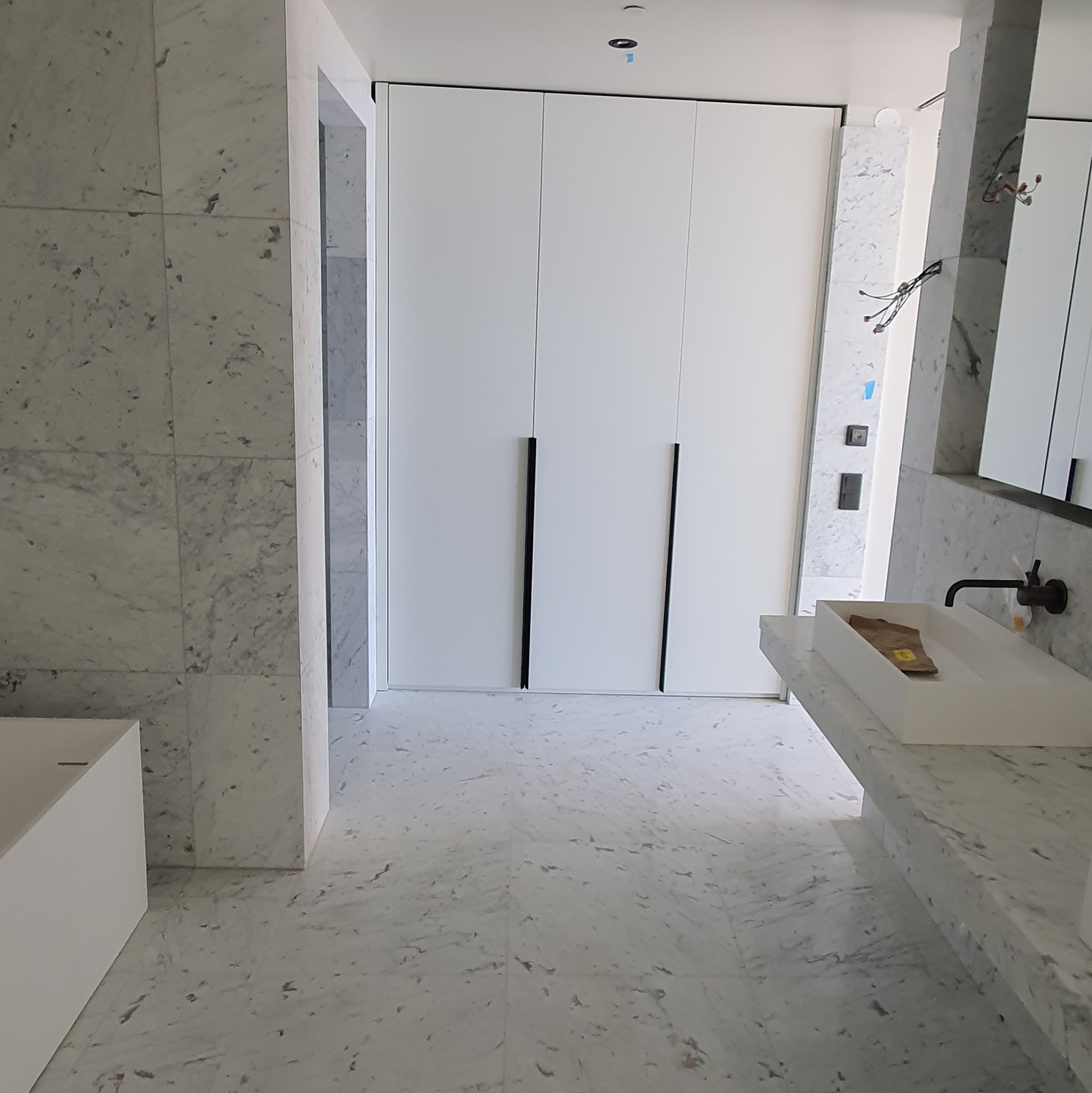 Elegancka łazienka w bieli i szarości z marmurowymi płytkami, minimalistyczną umywalką i zabudową szaf. Wnętrze po remoncie, widok na całe pomieszczenie.