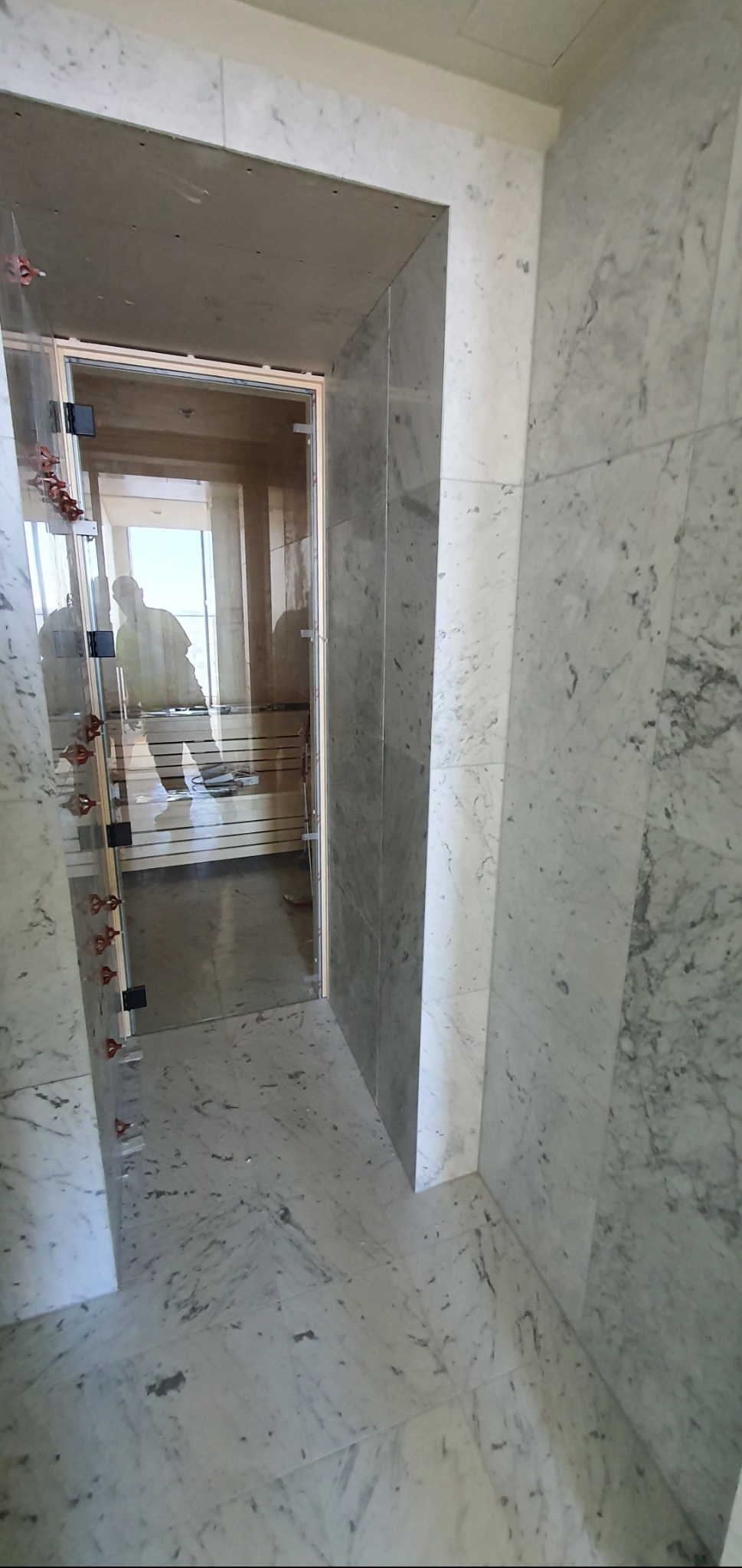 Łazienka w trakcie wykańczania: marmurowe płytki na ścianach i podłodze, zamontowana szklana kabina prysznicowa z widocznymi elementami montażowymi.