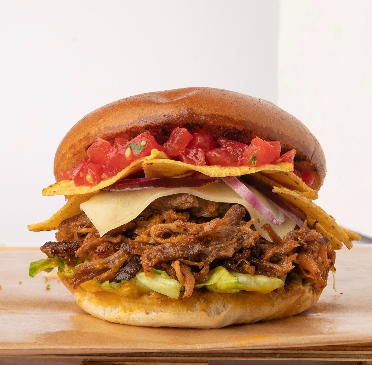 Apetyczny burger z szarpaną wieprzowiną, serem, nachosami i salsą pomidorową na jasnym tle. Widoczne warstwy składników.