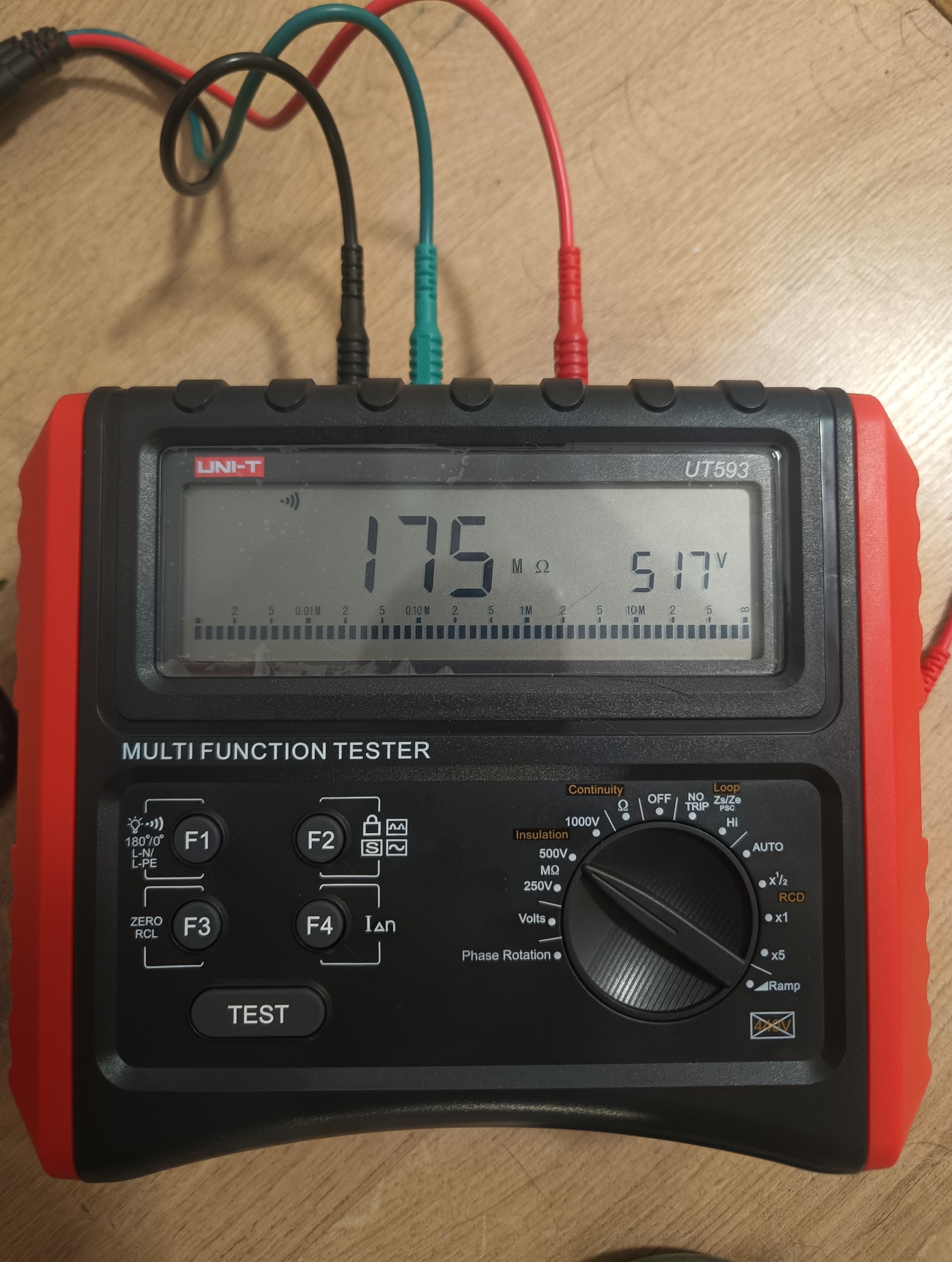 Miernik wielofunkcyjny Uni-T UT593 z podłączonymi przewodami pomiarowymi, wyświetlający wartości 175 mΩ i 517 V na tle drewnianej powierzchni.