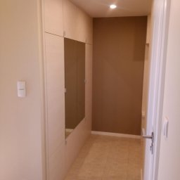 DWÓCH OD MEBLI Artur Sikorzyński - Jasna szafa wnękowa z lustrami w przedpokoju, oświetlenie sufitowe punktowe, beżowe płytki podłogowe, brązowa ściana w tle. Minimalistyczny design, neutralna kolorystyka.