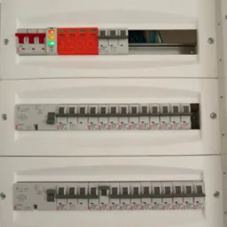 Rozdzielnia elektryczna z zabezpieczeniami przepięciowymi i wyłącznikami, widoczne bezpieczniki ETI, instalacja wewnątrz, oświetlenie LED.