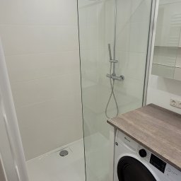 ARTEX - Nowoczesna łazienka z kabiną prysznicową typu walk-in, białe płytki i pralka pod blatem. Minimalistyczny design z chromowanymi detalami.