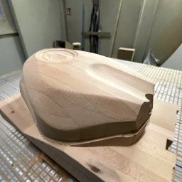 LAMDO SPÓŁKA Z OGRANICZONĄ ODPOWIEDZIALNOŚCIĄ - Drewniany model zbiornika paliwa motocykla, precyzyjnie wyfrezowany na stole roboczym z widocznymi śladami obróbki. Jasne drewno, neutralne tło warsztatu.