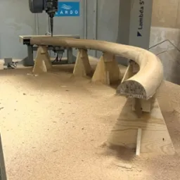 Drewniany, zakrzywiony element obrabiany na maszynie CNC Lambda ST, widoczne wióry, surowe drewno. Detal meblowy po frezowaniu.