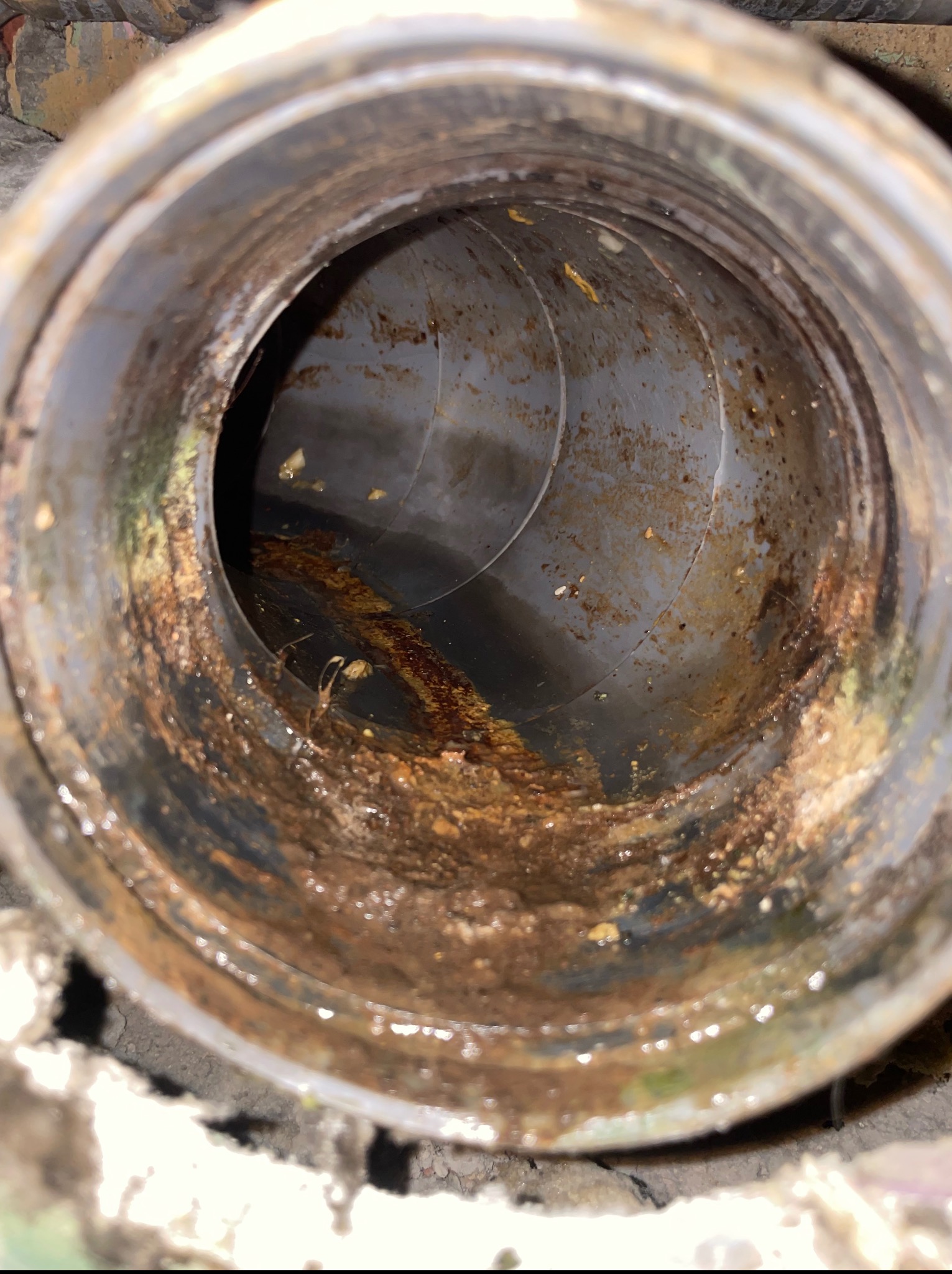 Wnętrze zanieczyszczonej, szarej rury kanalizacyjnej, widok z bliska. Osady i zabrudzenia wewnątrz, częściowo wypełnione płynem. Rura w trakcie udrażniania.