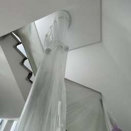 UBS - Schody i lampa zabezpieczone folią malarską w trakcie prac. Widok z dołu na białe wnętrze przed malowaniem. Zabezpieczenie przed zabrudzeniem.