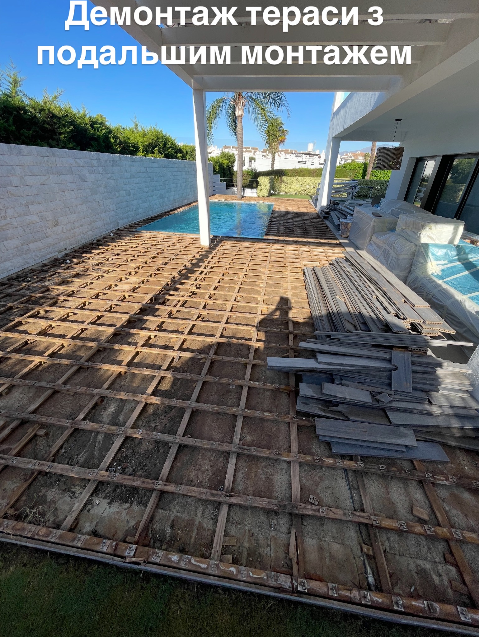 Demontaż drewnianej konstrukcji tarasu przy basenie, przygotowanie do montażu nowych desek tarasowych. Widoczny cień osoby wykonującej zdjęcie.